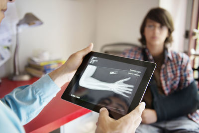 Cropped image of doctor examining hand x-ray with boy sitting in background