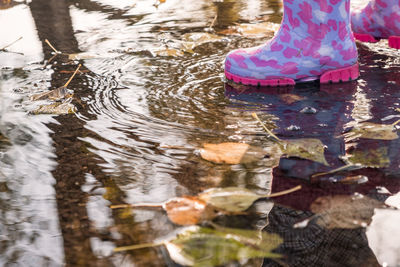 Low section of child wearing pink boot standing in puddle