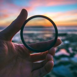 Close-up of hand holding sea against sky during sunset
