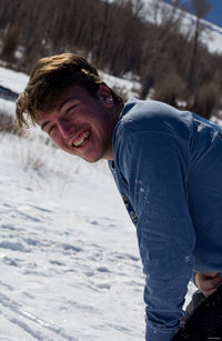 Portrait of cheerful young man standing on snow covered land