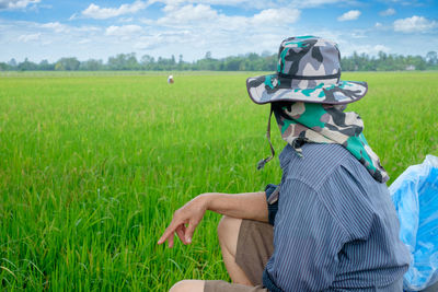 Man wearing hat looking away while sitting on agricultural field
