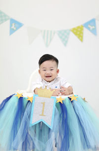 Portrait of cheerful baby boy sitting on table against bunting during birthday