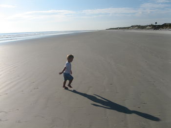 Side view of little boy playing with shadow at beach on sunny day