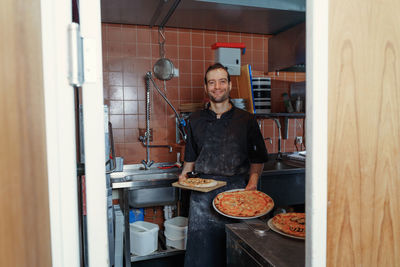 Portrait of young male chef preparing italian pizza in kitchen