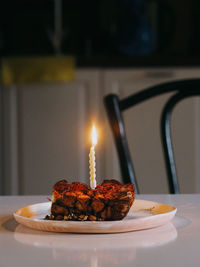 A slice of a cake with candle on a white ceramic plate