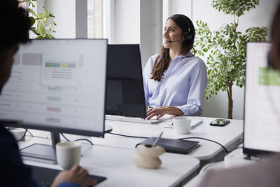 Smiling mid adult businesswoman using headset in office in front of computer screen