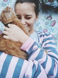 High angle view of smiling woman embracing cat on bed