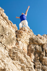 Low angle view of man standing on rock against clear sky
