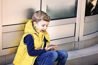 Full length of boy sitting on mobile phone