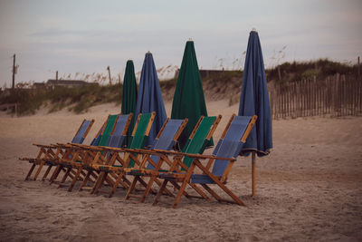 Empty chairs on beach against sky