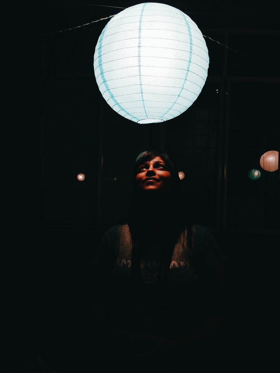 PORTRAIT OF SMILING YOUNG WOMAN AGAINST ILLUMINATED LIGHTS