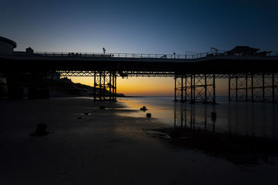 Silhouette bridge over sea against clear sky during sunset