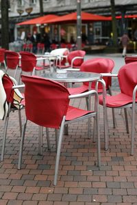 Empty chairs and tables at sidewalk cafe by building