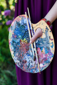 Midsection of woman holding palette and paintbrushes