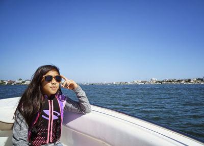 Beautiful teenage girl wearing sunglasses while sitting on yacht in sea