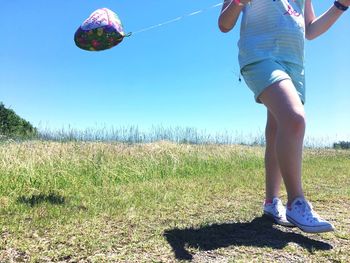 Low section of girl standing on field against clear blue sky