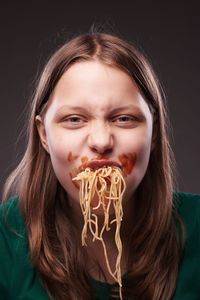 Portrait of young woman eating food against black background