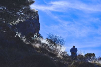 Rear view of silhouette woman standing on rock against blue sky