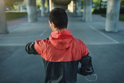 Rear view of man checking time while standing on street under bridge