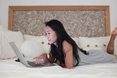 Woman using laptop while lying down on bed at home