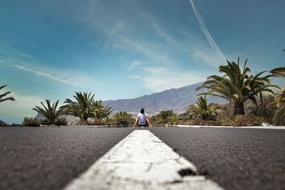 Rear view of man sitting on road against sky