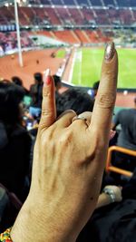 Cropped hand of woman gesturing horn sign in stadium