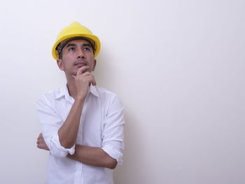 Young man looking away while standing against white wall