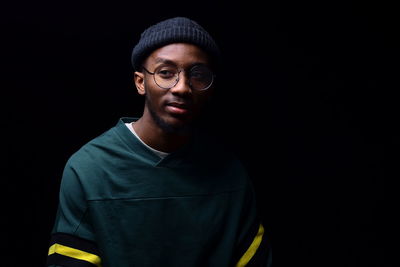 Portrait of young man standing against black background