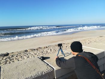 Rear view of man photographing sea against clear sky