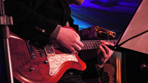 Midsection of man playing electric guitar during music concert