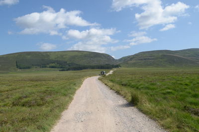 Vehicle on dirt road over green landscape against sky