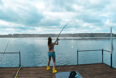 Rear view of man fishing in lake against sky