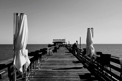 Pier leading to sea against clear sky