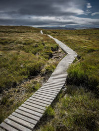 Footpath leading towards field against sky