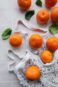 Mesh bag with oranges, tangerines on a pink tile background