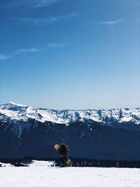 Snowboarder holding snowboard against blue sky