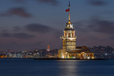 Illuminated buildings by sea against sky at night