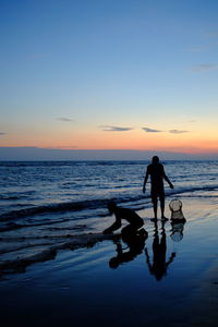 Silhouette people walking on beach against sky during sunset