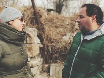 Man and woman wearing warm clothing while standing by stone wall