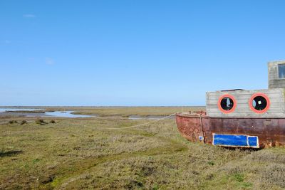 Abandoned building on field against clear blue sky