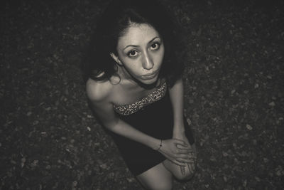High angle portrait of young woman crouching on street at night