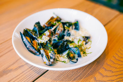 Close up of freshly cooked mussles in a plate with ingredients.