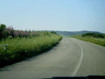 Road passing through field against clear sky