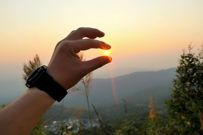 Midsection of person holding sun against sky during sunset