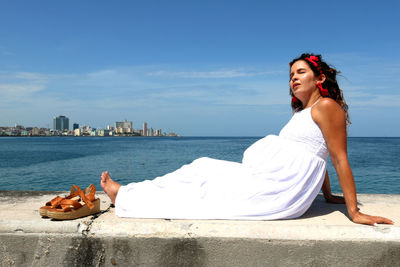 Woman sitting by sea against sky