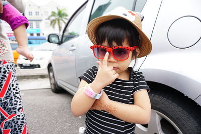 Cute girl wearing sunglasses and hat standing against car