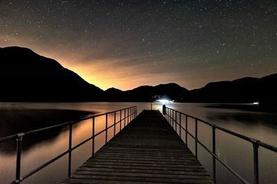 Pier over lake against sky at night