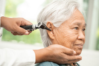 Audiologist or ent doctor use otoscope checking ear of asian senior woman patient 