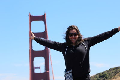 Portrait of smiling woman gesturing while standing against clear sky