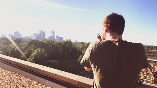 Rear view of man photographing city against sky